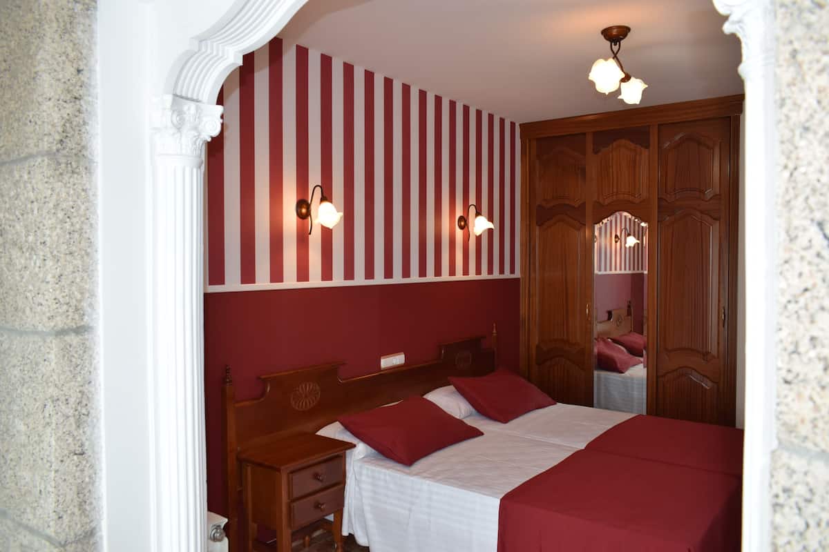 A bedroom with a bed, wooden headboard, two bedside tables, a nightstand, a mirror, and a wardrobe.