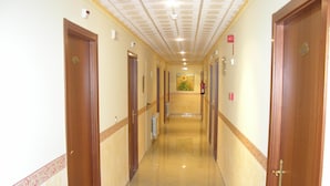 A long, narrow hallway with wooden doors on both sides, a tiled floor, and a ceiling with recessed lighting.