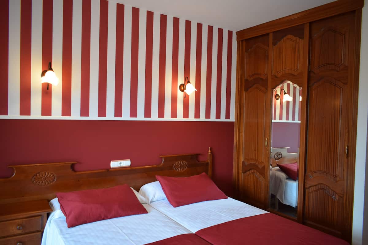A double bed with red and white bedding, a wooden headboard, and two wall-mounted lights.
