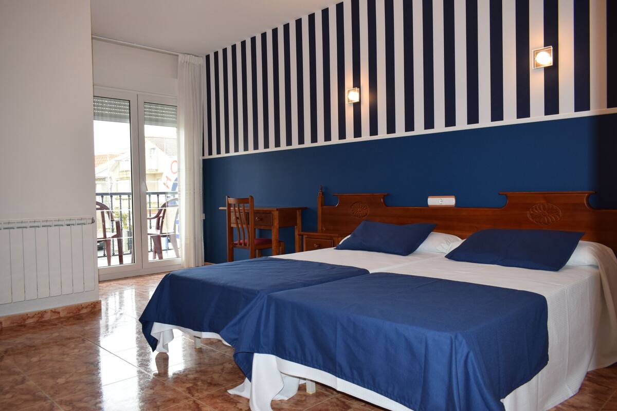 A hotel room with two beds, a wooden headboard, a small table, and a chair.