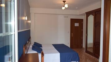 Een hotelkamer met een bed, een houten garderobe, een spiegel en een plafondlamp.