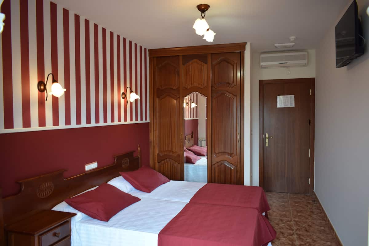 A hotel room with a large bed, wooden wardrobe, and a television on the wall.