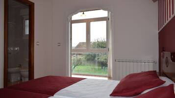 Un dormitorio con cama, ventana y baño visible a través de una puerta abierta.