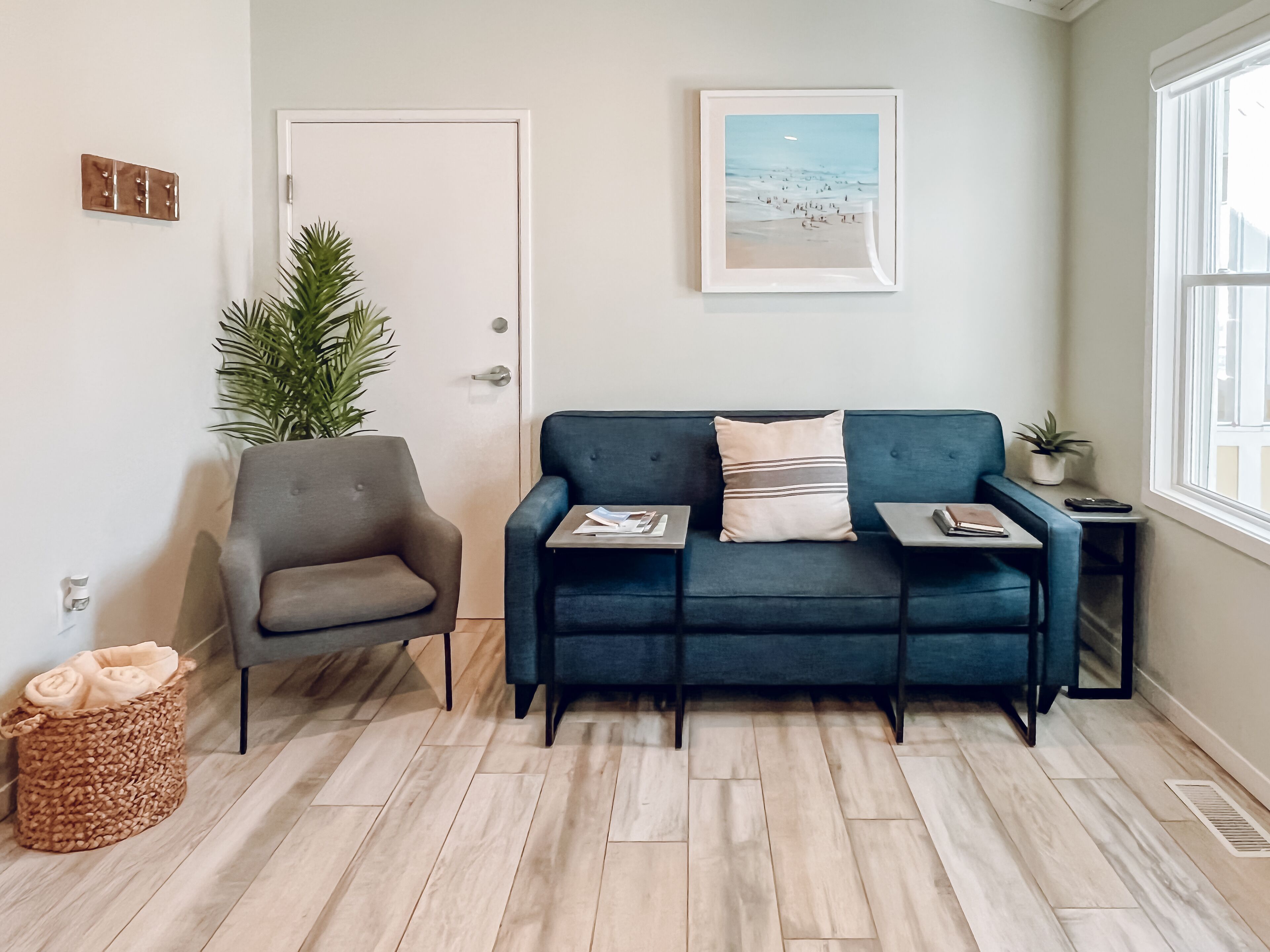 A modern living room with a grey armchair, a blue sofa, and a small table with a plant and a remote control.