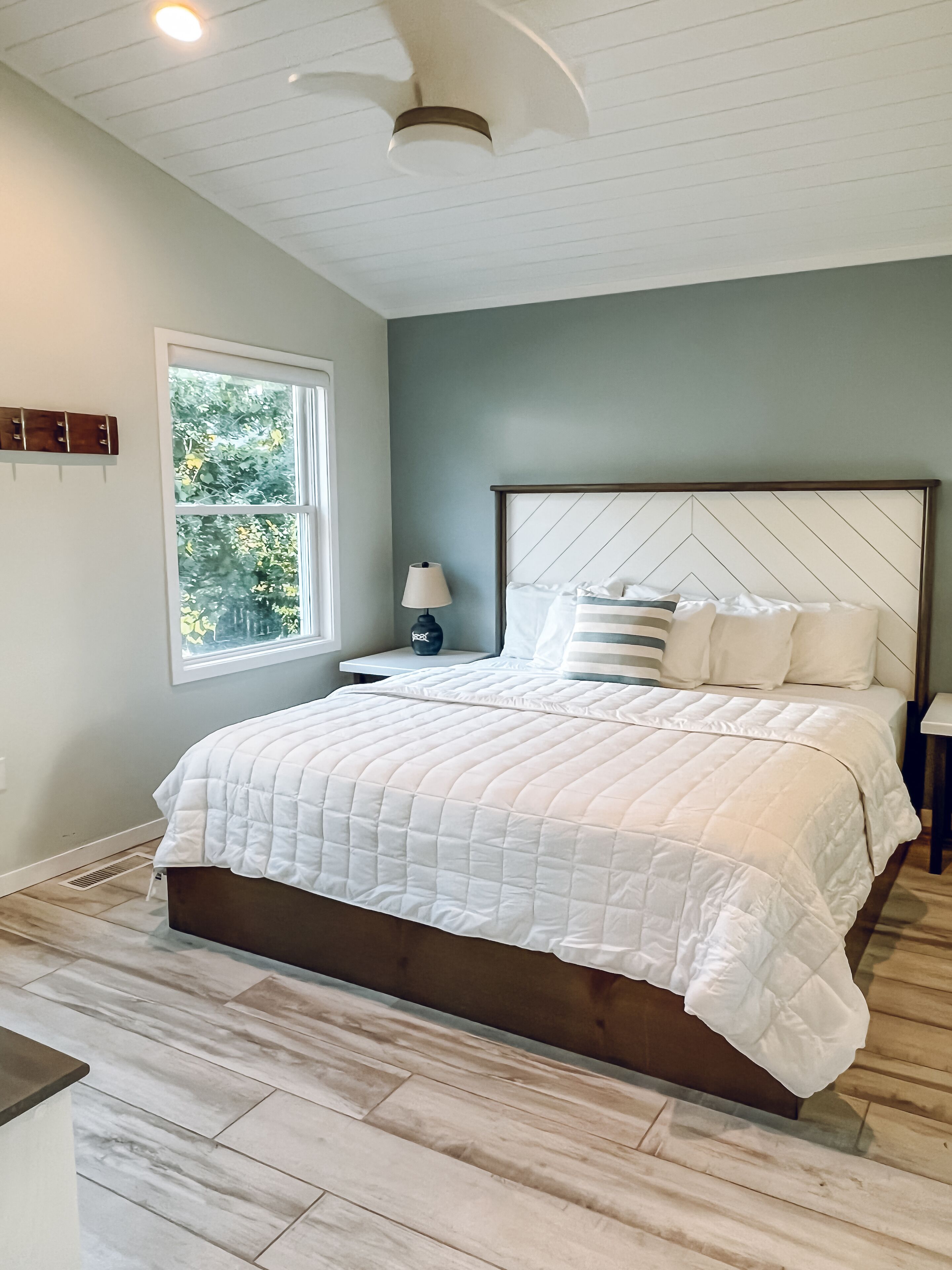 Quarto com uma cama grande, mesa de cabeceira, janela e ventilador de teto.