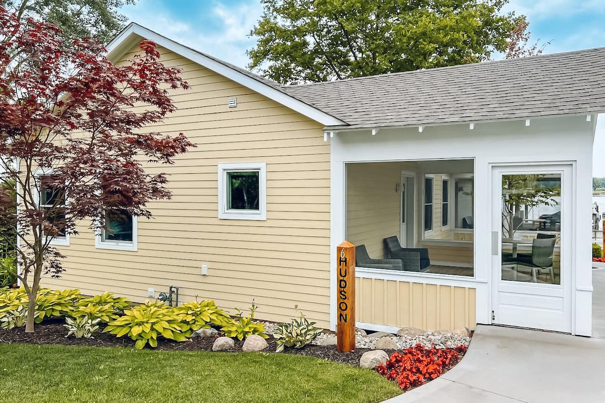 A modern house with a covered porch, a small garden with various plants, and a clear sky.