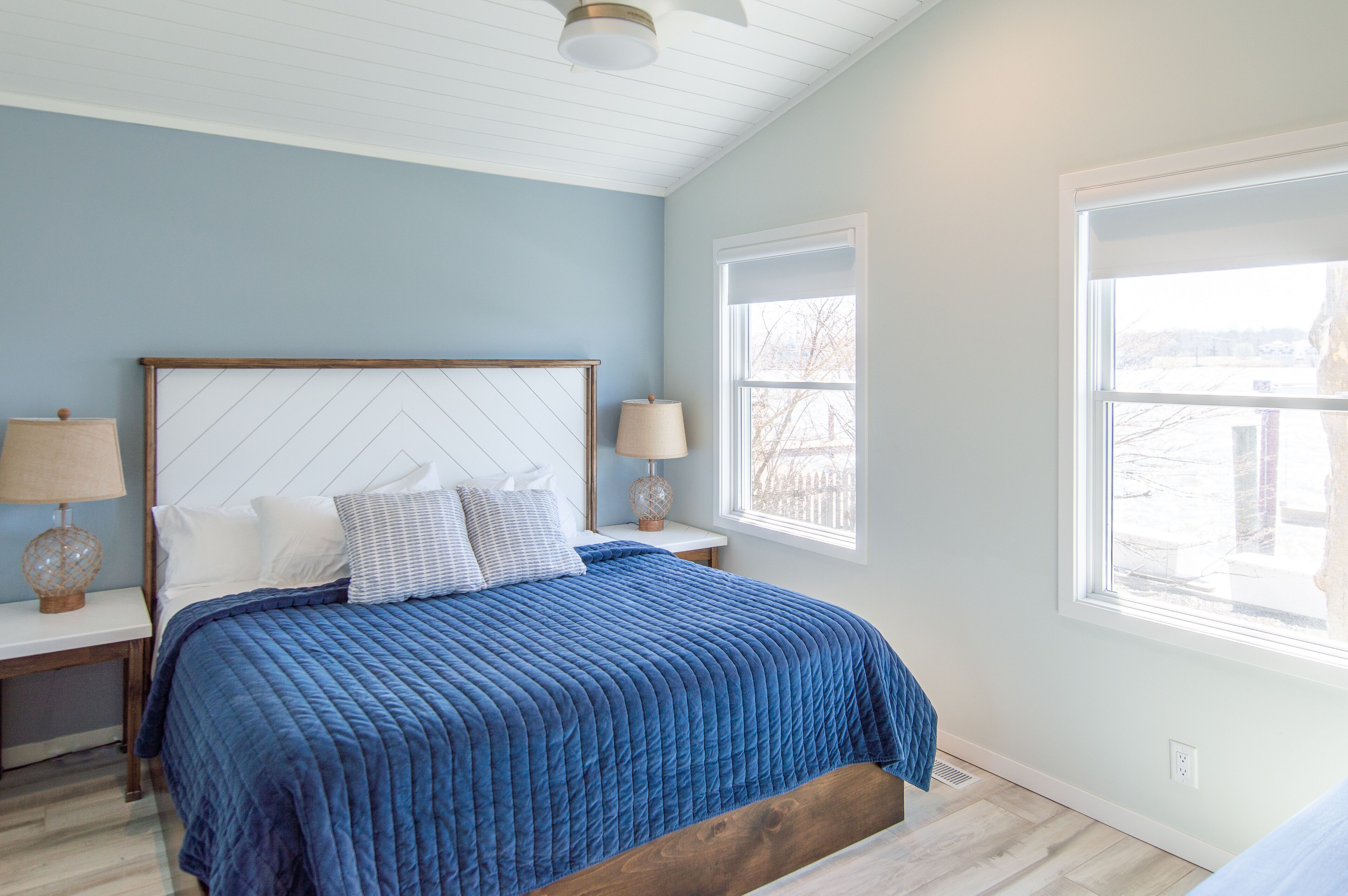 A bedroom with a bed, nightstands, and two windows.