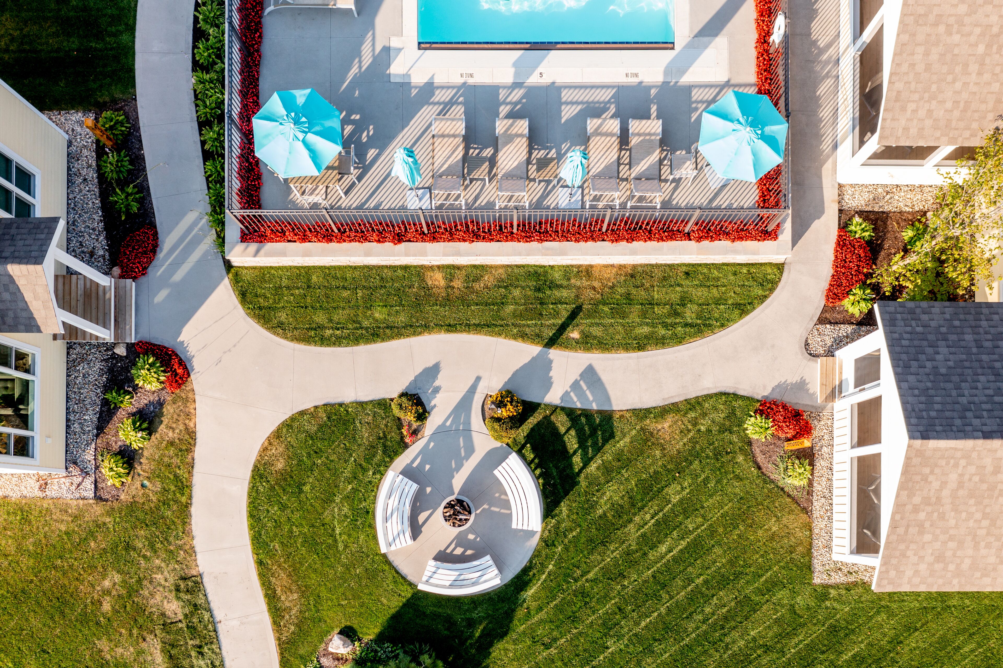 An aerial view of a residential area with a swimming pool, outdoor seating, and landscaped gardens.