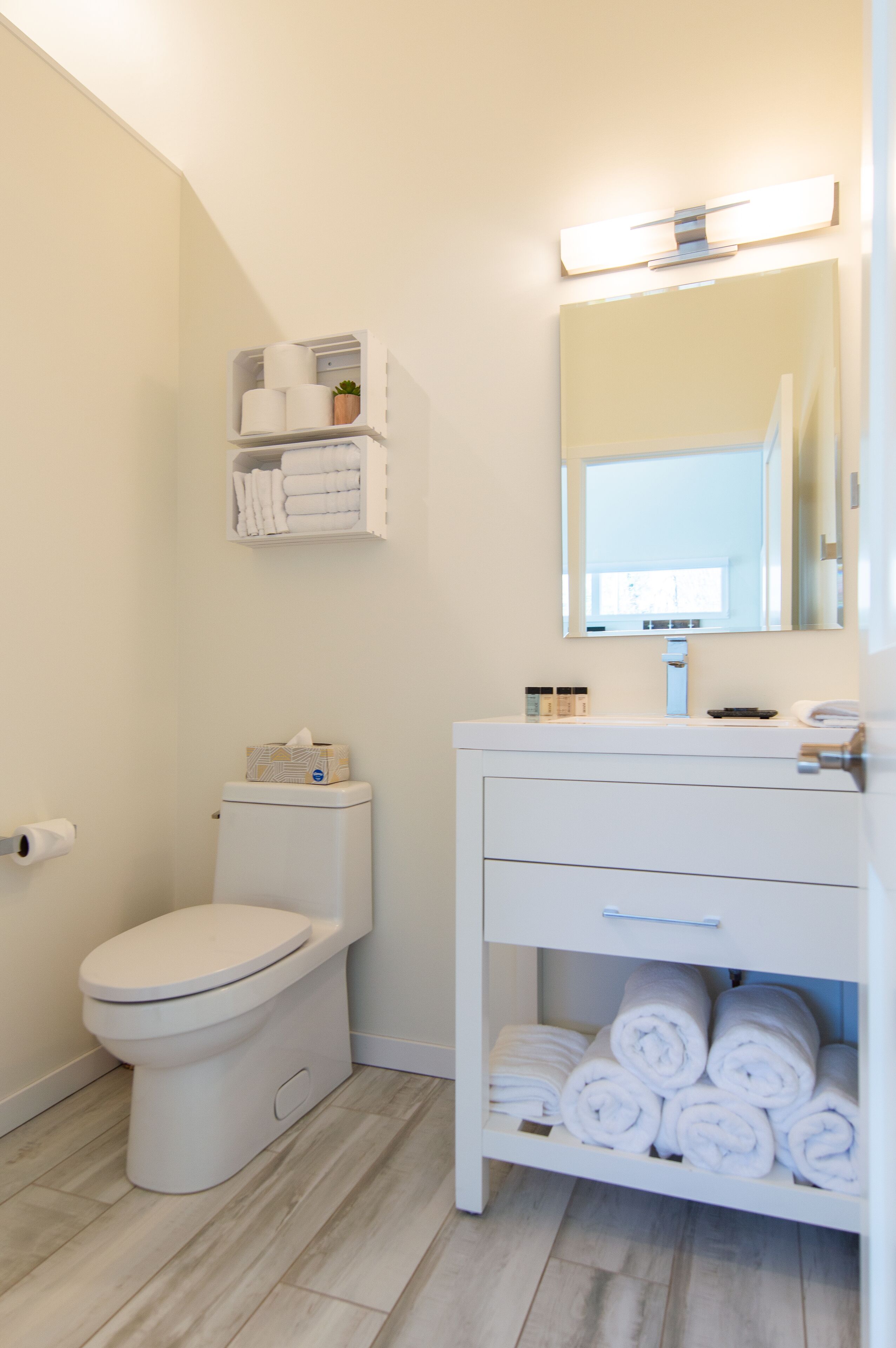 A bathroom with a toilet, a sink with a mirror, and shelves with towels.