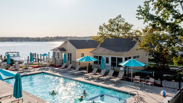 A swimming pool with lounge chairs and umbrellas, a dock with a boat, and a house with a view of the water. - Old Pike Cottages (Saugatuck)