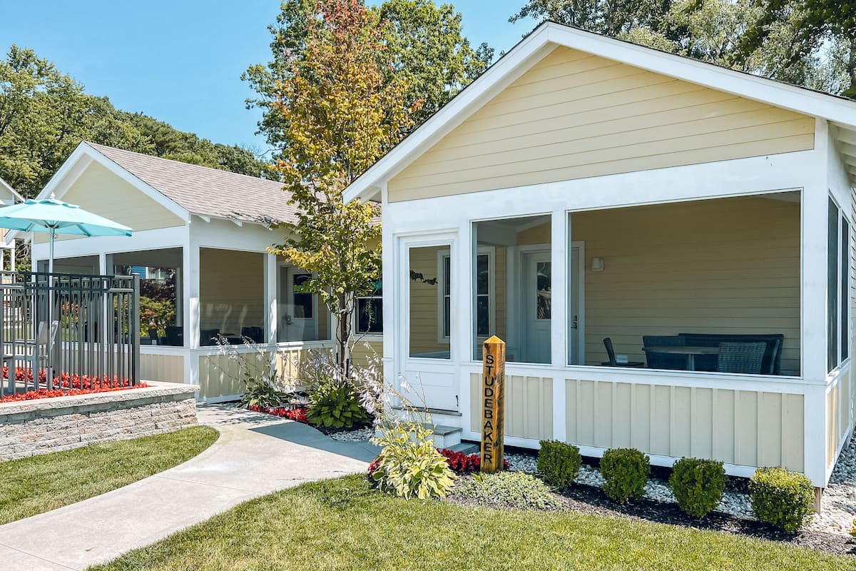 A white mobile home with a porch, a small garden, and a wooden sign.