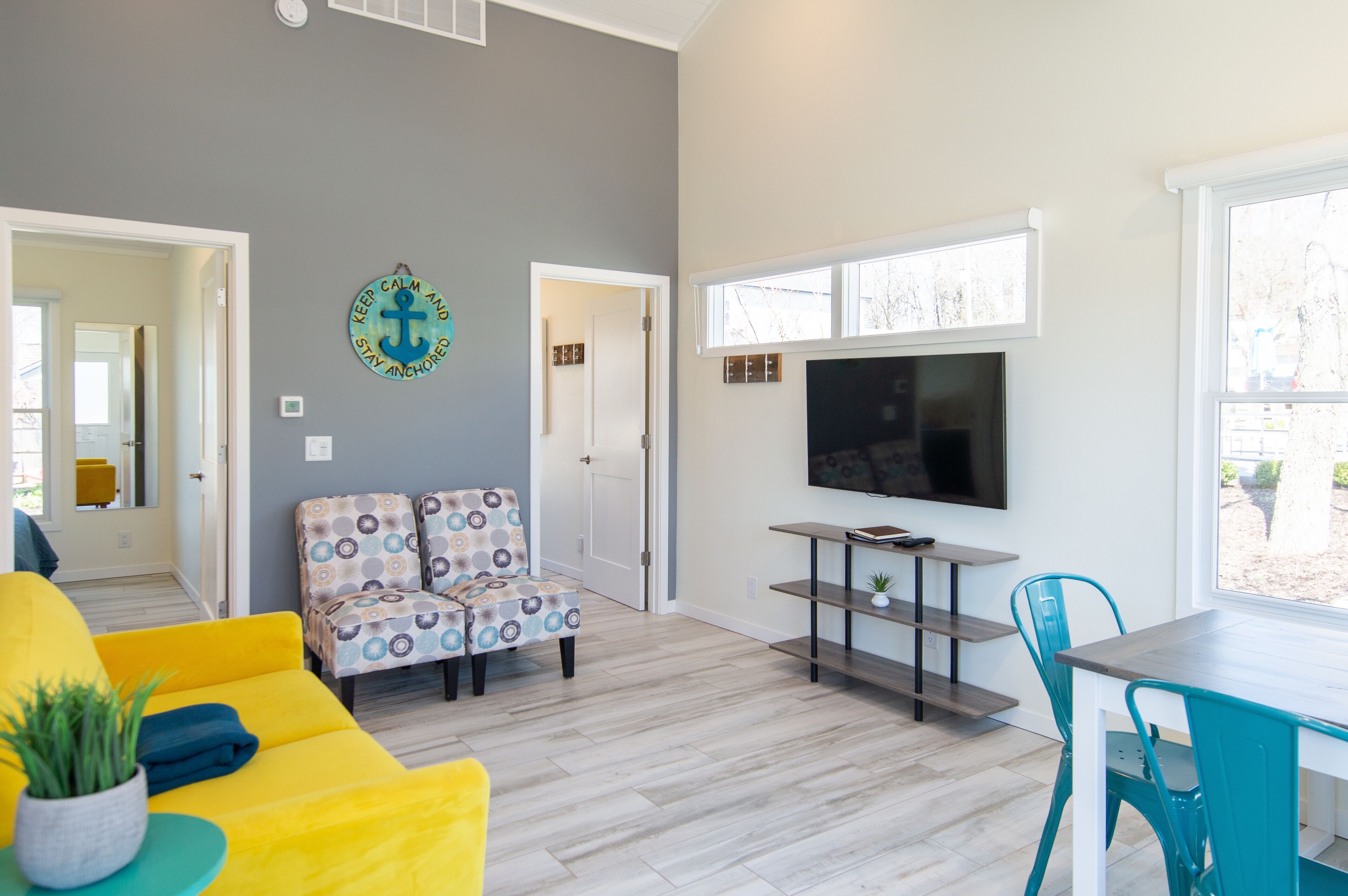 Una sala de estar con un sofá amarillo, un sillón estampado y un televisor montado en la pared.