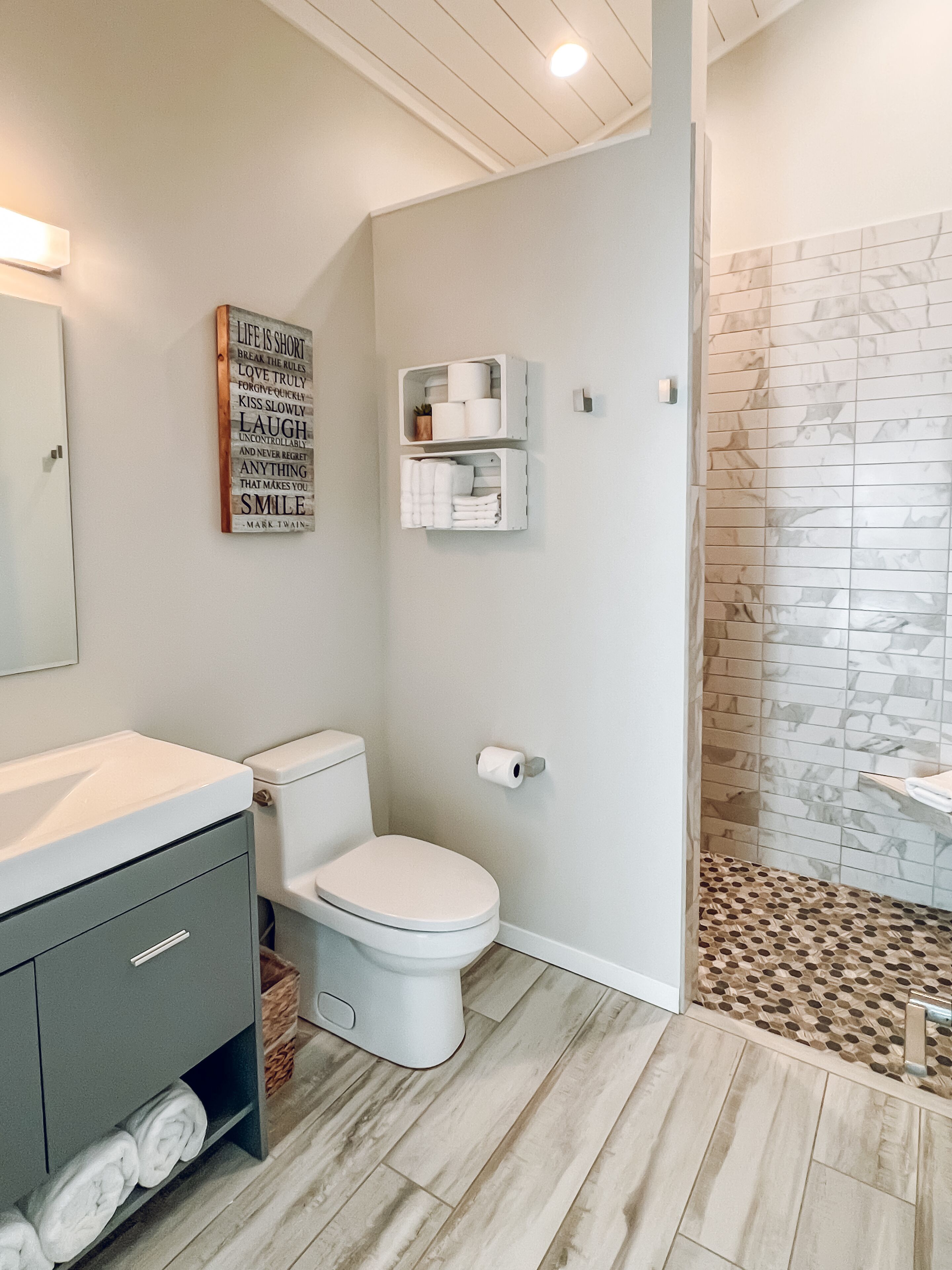 A modern bathroom with a toilet, a vanity with a mirror, and a shower area with a patterned floor.
