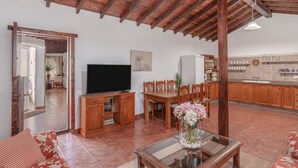 A spacious living area with a wooden ceiling, a television, a dining table with chairs, and a kitchen in the background. - Villa "Abraham" with Mountain View, Wi-Fi, Pool & Terrace (Tefía)