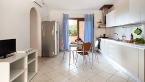 Eine moderne Küche mit weißen Schränken, einem Esstisch mit Stühlen, einem Fernseher und einem Kühlschrank.