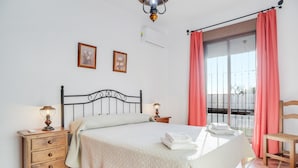 A bedroom with a bed, bedside tables, a chair, a balcony with curtains, and two wall-mounted pictures.