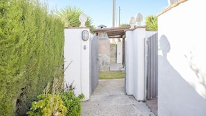 A narrow pathway leading to a gated entrance with a stone wall and a metal gate.