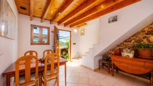 Un área de comedor con sillas de madera y una mesa, una escalera con pared de piedra y vistas al exterior.