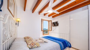 Un dormitorio con una cama, ventilador de techo, televisión y ventana.