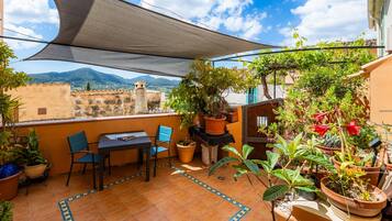 A terrace with a table and chairs, potted plants, and a view of mountains.