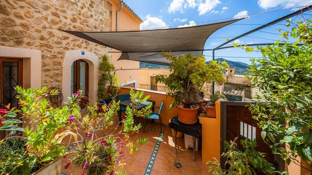Un edificio de piedra con patio, mobiliario exterior y plantas en macetas.