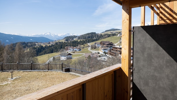 A wooden balcony with a view of a village and mountains. - Holiday Apartment "Wohnung 5" with Sauna, Terrace & Mountain View (Terenten)