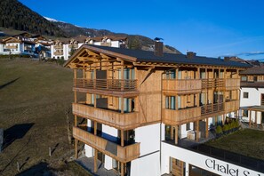 Eine mehrstöckige Holzhütte mit Balkonen, ein Skilift im Hintergrund und ein klarer Himmel.