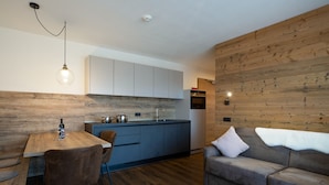 A modern kitchen with wooden cabinetry, a dining area with a table and chairs, and a grey sofa. - Holiday Apartment "Wohnung 5" with Sauna, Terrace & Mountain View (Terenten)