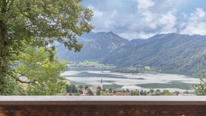 A scenic view of a mountainous landscape with a lake, a church, and a town in the valley. - Vacation on a Farm - Fantastic Holiday App with Balcony, Garden, Lake & Mountain View (Schliersee)