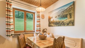 A dining area with a wooden table, chairs, a bowl, and a painting of a mountain landscape. - Vacation on a Farm - Fantastic Holiday App with Balcony, Garden, Lake & Mountain View (Schliersee)