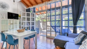 A spacious living area with a large sliding glass door, a white dining table with chairs, a sofa, and a television on a white cabinet. - Modern apartment with garden, air conditioning and Wi-Fi (LACONA - CAPOLIVERI (LIVORNO))