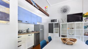 A modern kitchen with white cabinets, a built-in microwave, and a dining area with a white table and blue chairs. - Modern apartment with garden, air conditioning and Wi-Fi (LACONA - CAPOLIVERI (LIVORNO))