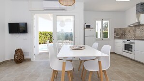 A modern kitchen with white cabinets, a built-in oven, and a dining area with a white table and chairs. - Air-Conditioned Holiday Home on the Beach with Pool, Terraces & Wi-Fi (Ciutadella de Menorca)