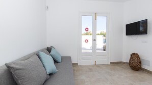 A room with a grey sofa, a television mounted on the wall, and a door with a view of the outside. - Air-Conditioned Holiday Home on the Beach with Pool, Terraces & Wi-Fi (Ciutadella de Menorca)