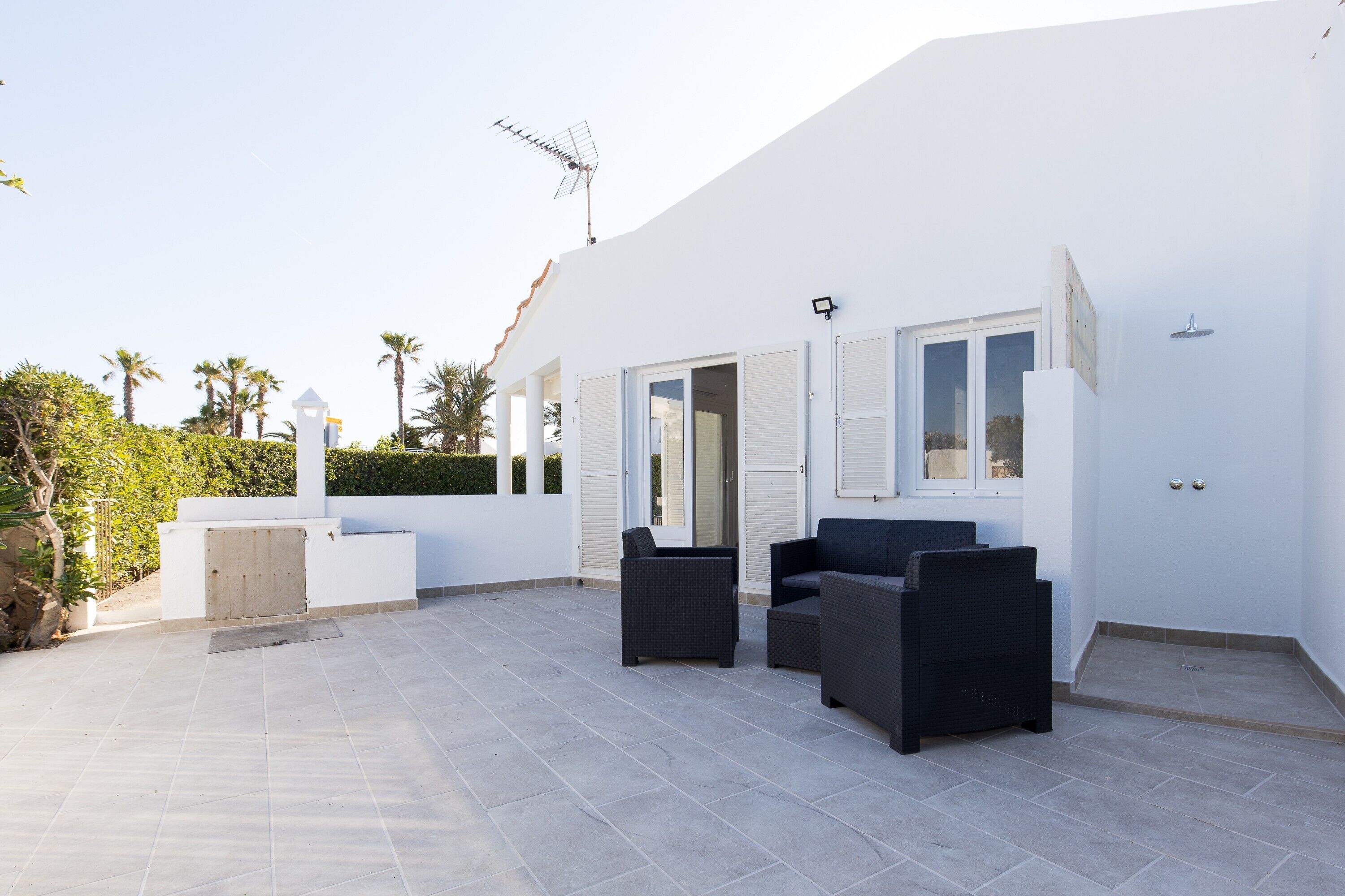 Un edificio blanco con un patio que incluye dos sillas de mimbre negro y una mesita.