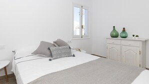 A bedroom with a bed, a bedside table, a window, and a cabinet with decorative items. - Air-Conditioned Holiday Home on the Beach with Pool, Terraces & Wi-Fi (Ciutadella de Menorca)