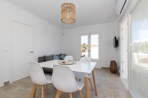 A modern dining area with a white table and chairs, a wicker pendant light, and a view through a glass door.