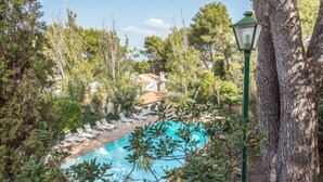 Zona de piscina con sillas de descanso, rodeada de árboles y un farol.