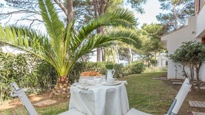 Una mesa al aire libre con mantel blanco, una jarra, tazas y un plato de comida.
