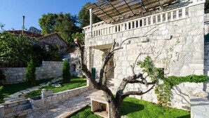Un bâtiment en pierre doté d’un espace extérieur couvert, d’un chemin en pierre et d’un arbre au premier plan.