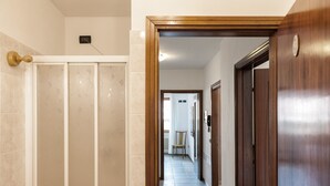 A hallway with a shower, a wooden door, and a chair in the distance.