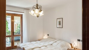 A bedroom with a bed, a bedside table, a chandelier, a door leading to a balcony, and a framed picture on the wall.