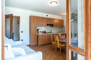 A compact kitchen with wooden cabinets, a dining table with chairs, and a kitchenette area. - Bright and comfortable - Appartamento Aria (Tignale)