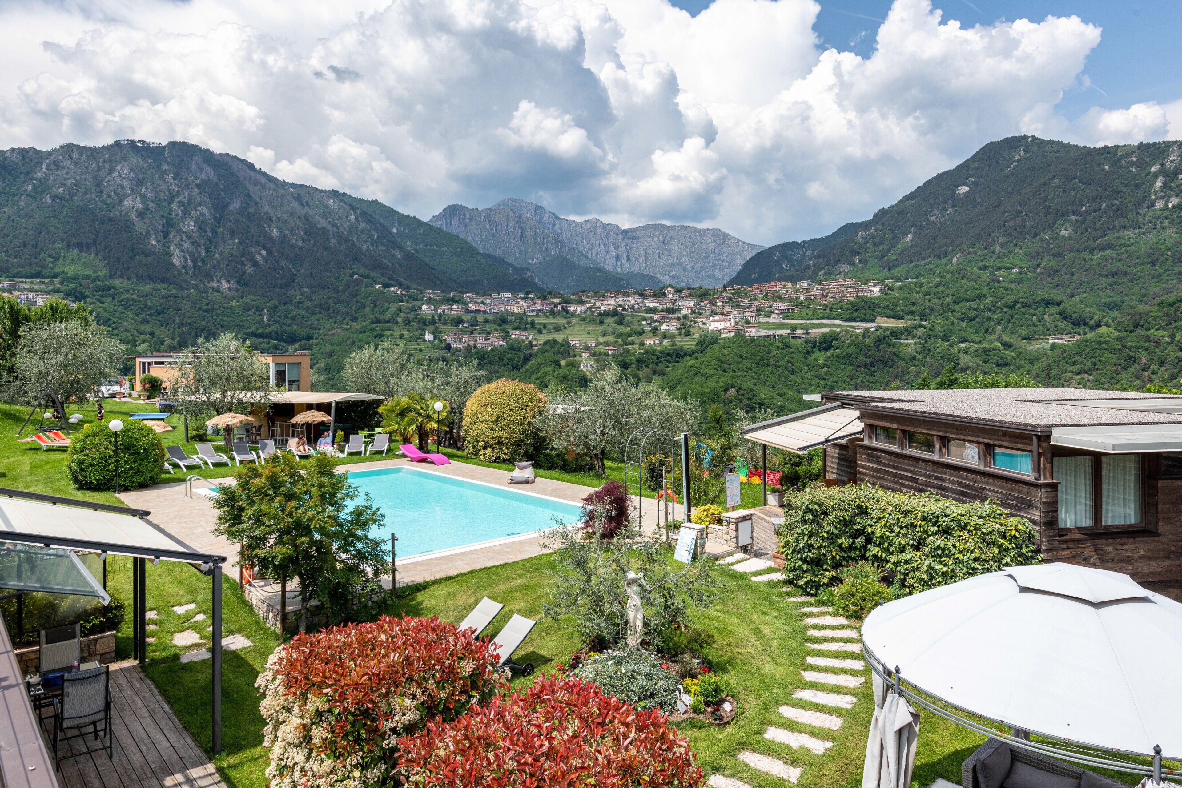 Una piscina con montagne sullo sfondo, un'area patio e vista su un paese.