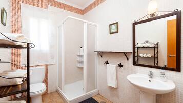 Ein Badezimmer mit Toilette, einer Dusche mit Glaswand, einem Waschbecken mit Spiegel und einem Handtuchhalter.