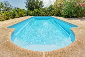 Una piscina rectangular con agua azul cristalina, rodeada por una terraza de piedra.