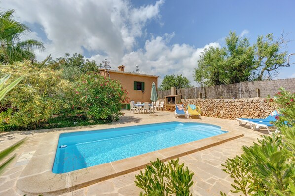 A swimming pool with a stone deck, a small building, and a stone wall.