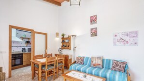 A cozy living room with a wooden sofa, a dining table, and chairs. A kitchen is visible through an open doorway. - Country house "Sa Barraca d'en Camine" with pool in the nature (portopetro)