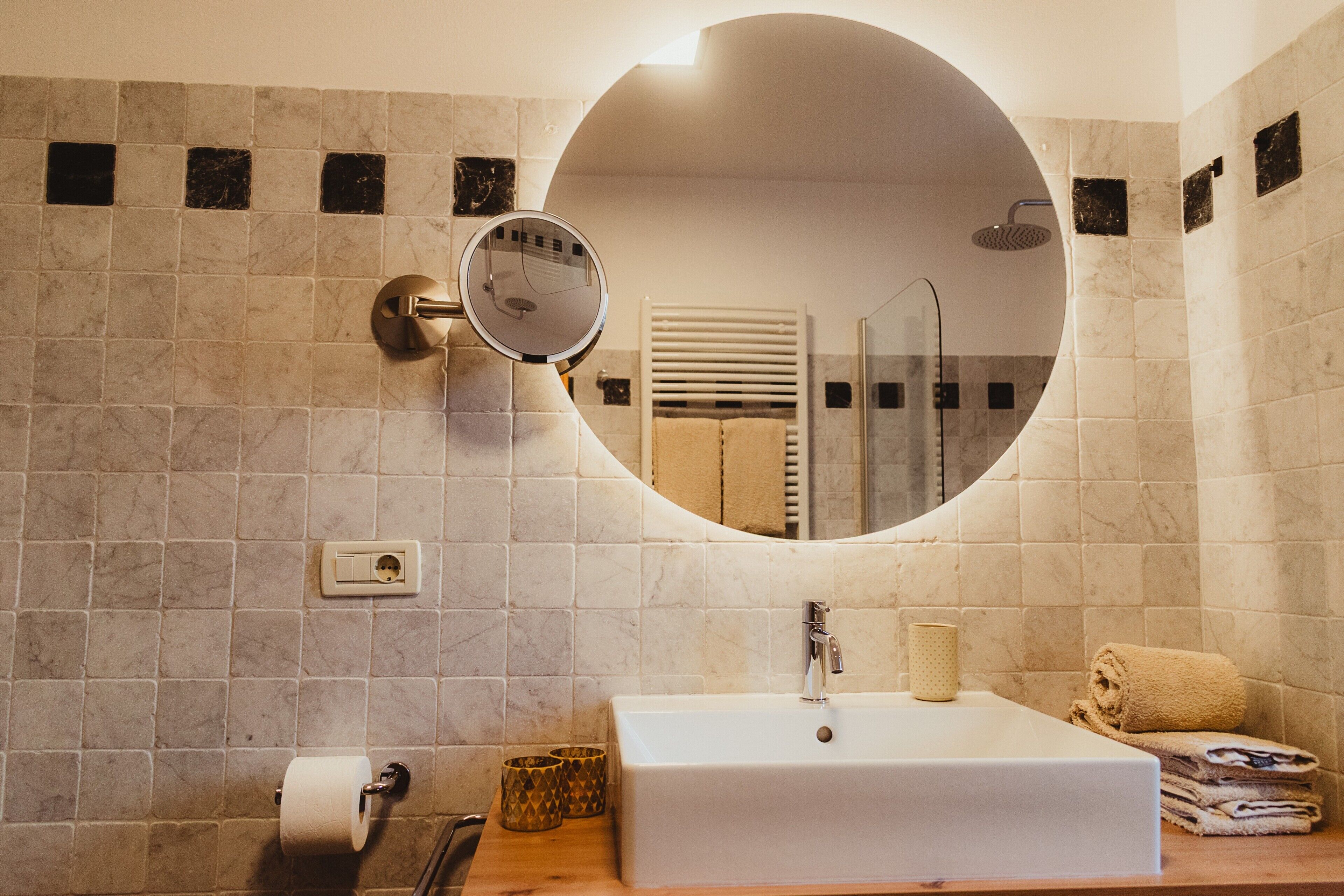 Un baño con un espejo redondo, un lavabo, una toalla y una ducha.