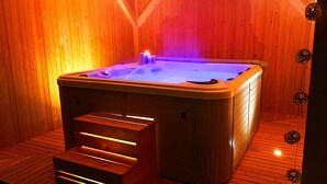 En bastu byggd av trä, med ett bubbelbad, en träbänk och ett tak med synliga träbjälkar.